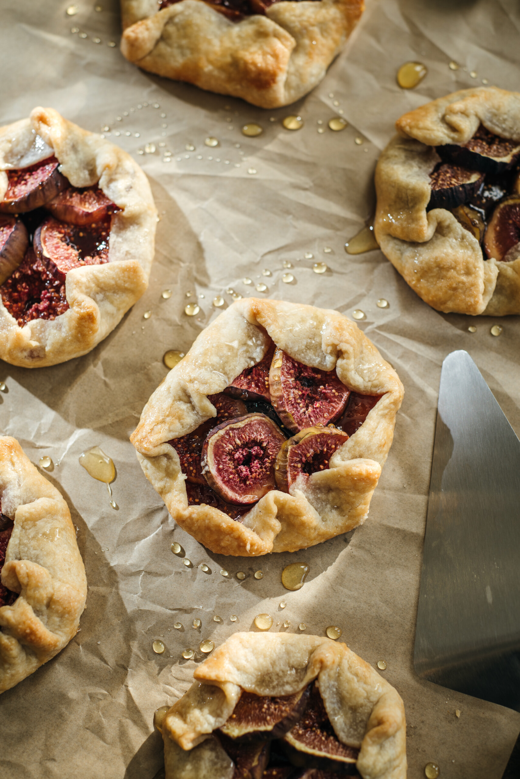 A batch of mini fig galettes with flaky pastry and roasted figs on top, glistening with honey on parchment paper.
