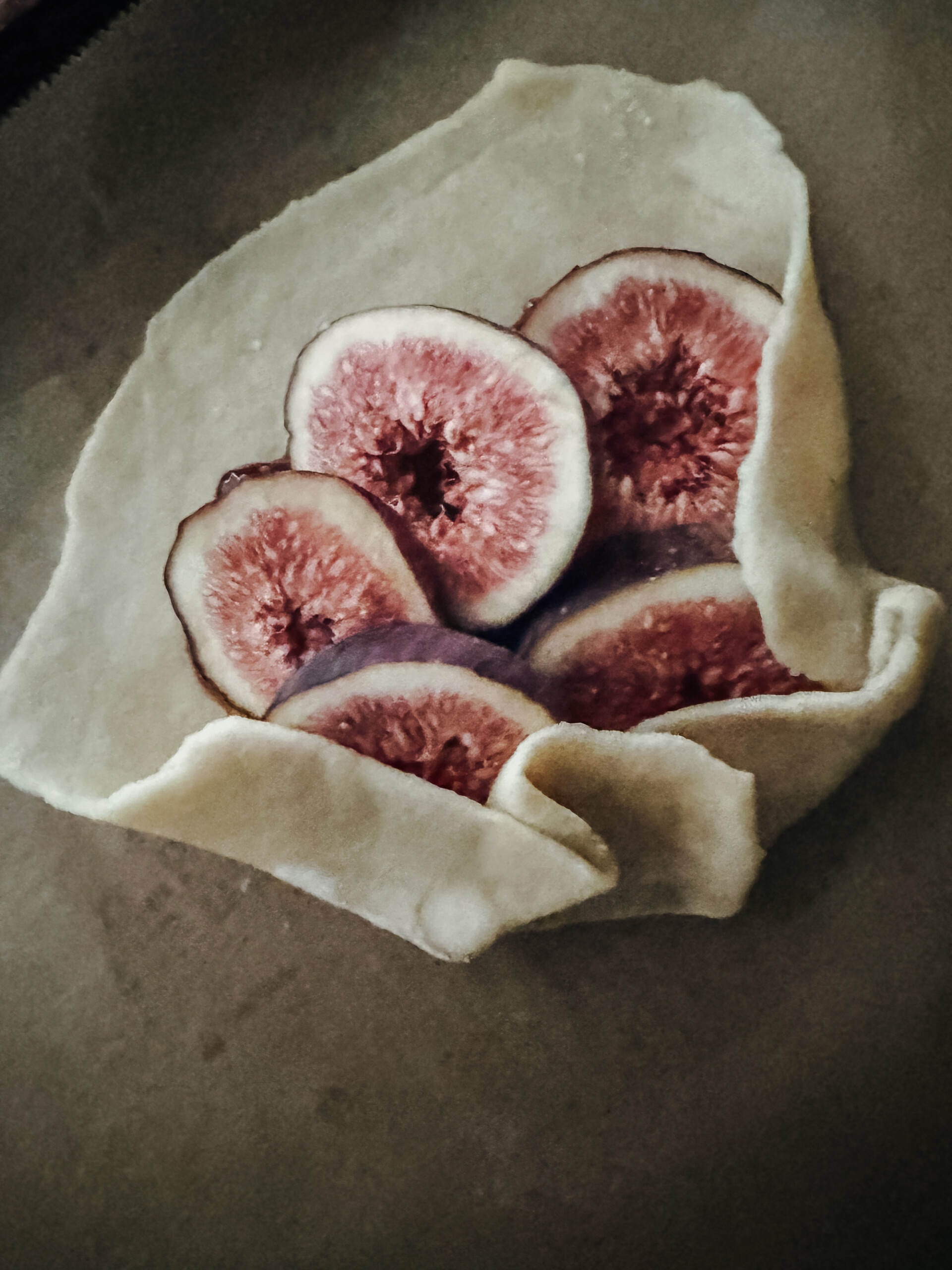 Unbaked fig galette with fresh fig slices arranged on dough, edges being folded over to form a rustic tart shape.
